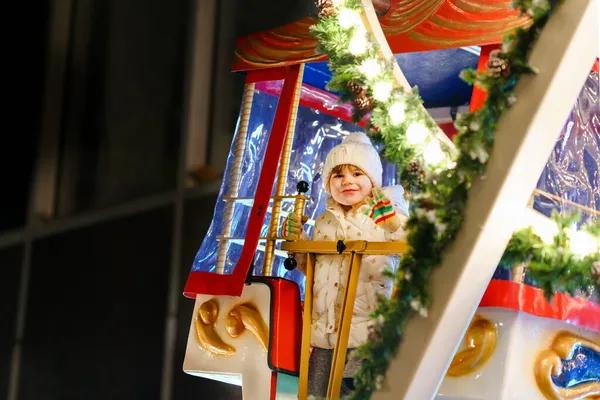 Pequena menina pré-escolar montando no cavalo carrossel roda gigante na feira de Natal ou mercado, ao ar livre. Criança feliz se divertindo no mercado tradicional de xmas de família na Alemanha — Fotografia de Stock