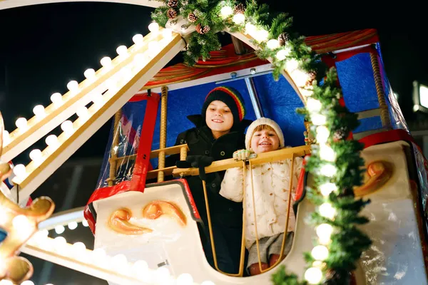 Dziewczynka z przedszkola i uczeń jadący na koniu karuzelowym na jarmarku lub targu świątecznym, na świeżym powietrzu. Dwójka szczęśliwych dzieci bawiących się na tradycyjnym rodzinnym rynku świątecznym w Niemczech — Zdjęcie stockowe