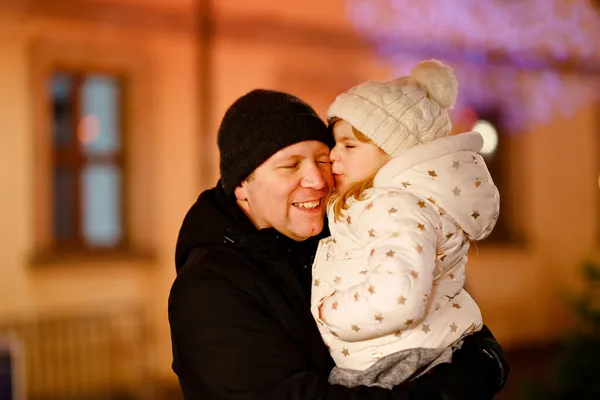 Little preschool girl sitting on shoulder of father on Christmas market in Germany. Happy toddler child and man observing traditional decorated pyramid. Happy family, bonding, love. Family xmas time. — Stock Photo, Image