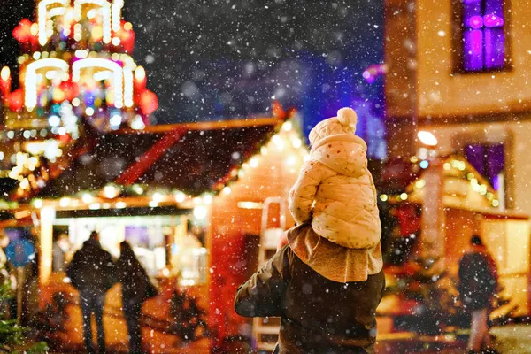 Little preschool girl sitting on shoulder of father on Christmas market in Germany. Happy toddler child and man observing traditional decorated pyramid. Happy family, bonding, love. Family xmas time. — Stock Photo, Image