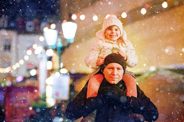 Little preschool girl sitting on shoulder of father on Christmas market in Germany. Happy toddler child and man walking on the streets of German festive city. Family, bonding, love. Family xmas time. — Stock Photo, Image