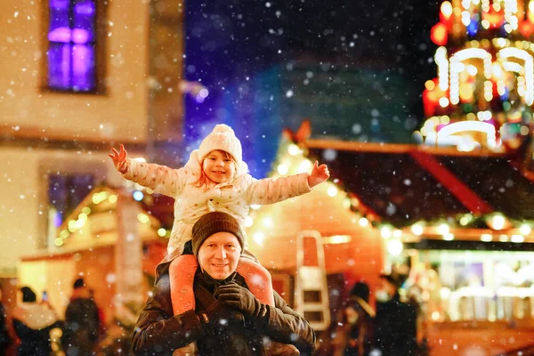 Niña preescolar sentada en el hombro de su padre en el mercado de Navidad en Alemania. Feliz niño y hombre observando la pirámide decorada tradicional. Familia feliz, unión, amor. Tiempo de Navidad en familia. — Foto de Stock