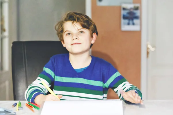 Portret van een leuke, vrolijke schooljongen die thuis huiswerk maakt. Schrijven met kleurrijke potloden, binnen. Basisschool en onderwijs. Kinderen die letters en cijfers leren schrijven — Stockfoto