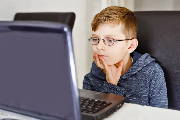 Glücklicher gesunder Junge mit Brille, der zu Hause mit dem Notizbuch Hausaufgaben macht. Interessiertes Kind schreibt Essay mit Hilfe des Internets. Konzentriertes Schulkindkonzept — Stockfoto