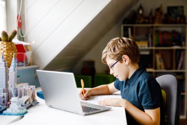 Gözlüklü çocuk evde okulda laptopta öğreniyor. Ev ödevi yapan, defter ve modern aletler kullanan sevimli bir çocuk. Evde eğitim kavramı.