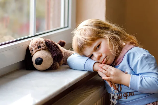 Overstuur peuter meisje zit bij het raam en kijkt uit. Triest huilend kind dat zich ongelukkig voelt. Opsluiting en isolatie concept tijdens de corona virus pandemie tijd. Eenzame kleuter. — Stockfoto