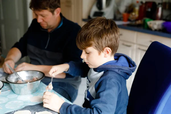 Šťastný blonďatý školák, který připravuje knedlíky s mletou kuchyní, uvnitř. Vtipné krásné zdravé dítě baví s vařením. Malý pomocník s otcem společně. — Stock fotografie