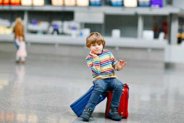 Uluslararası havaalanındaki terminalde büyük bavulları olan küçük mutlu çocuk. Okul öncesi heyecanlı çocuk uçuşu ve tatile çıkmayı bekliyor. Seyahat aile hayatı..