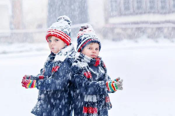 Two happy little kid boys in colorful fashion clothes playing outdoors during strong snowfall. Active leisure with children in winter. Funny preschool siblings and twins having fun with first snow — 图库照片