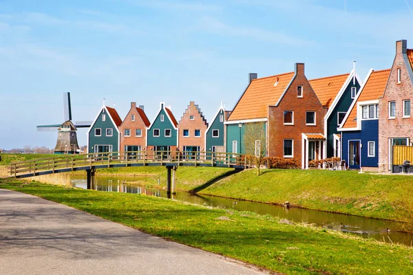 Panorama with modern brick houses along water in a family friendly suburban neighborhood in Volendam in the Netherlands. Typical Dutch houses and windmill on background. — Stock Photo, Image