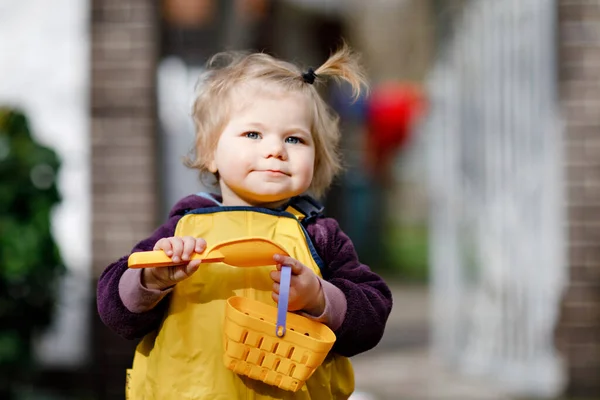 Niedliche entzückende Kleinkind Mädchen spielen mit Sand und Schaufel am Frühlingstag. Baby in gelben Stiefeln und Schlammpfützenhosen. Glückliches Mädchen pflanzt Gemüse im Frühling. — Stockfoto