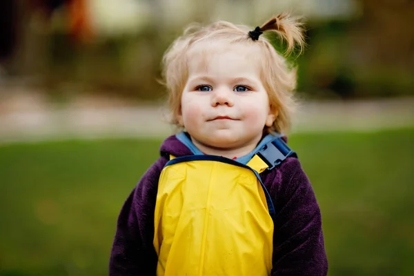 Söt söt liten flicka som leker utomhus på vårdagen. Baby barn bär gula lera regn pöl byxor byxor. Porträtt av lycklig flicka. — Stockfoto