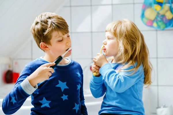 Niña preescolar y niño preadolescente cepillándose los dientes. Hermano enseñando a hermana a cepillar dientes. Felices hermanos. Dos niños divirtiéndose con la rutina dental matutina. Familia en interiores. — Foto de Stock