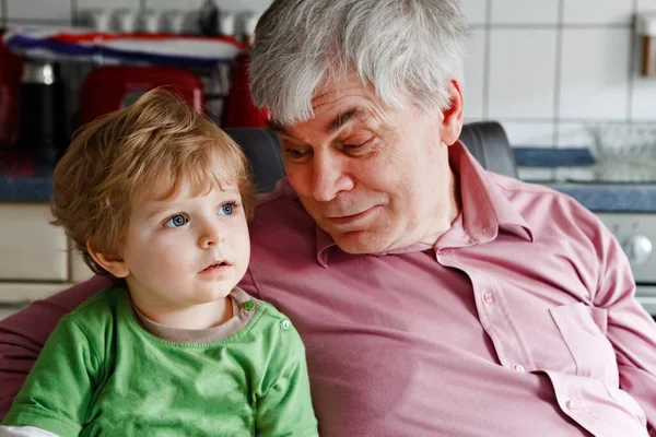 Little toddler boy and grandfather watching tv together. Happy family, grandchild and senior man, granddad at home, watch cartoons on television, indoors. — Stock Photo, Image