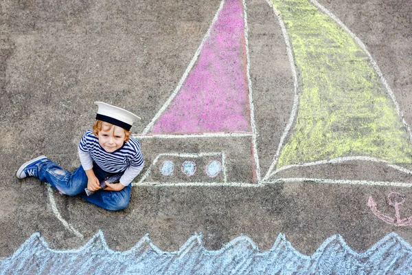 Petit garçon comme pirate sur le bateau ou voilier peinture d'image avec des craies colorées sur asphalte. Loisirs créatifs pour les enfants à l'extérieur en été. Enfant avec chapeau de capitaine et jumelles . — Photo