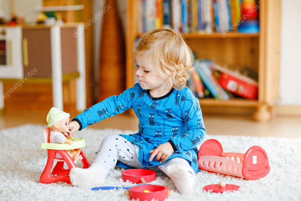 Adorable cute little toddler girl playing with doll. Happy healthy baby child having fun with role game, playing mother at home or nursery. Active daughter with toy.