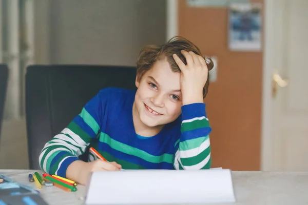 Ritratto di carino ragazzo della scuola felice a casa a fare i compiti. Bambino che scrive con matite colorate, al chiuso. Scuola elementare e istruzione. Kid imparare a scrivere lettere e numeri — Foto Stock