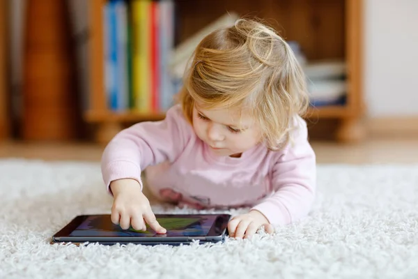 Sevimli küçük yürümeye başlayan çocuk kız evde tablet pc ile oynuyor. Yüzeye parmaklarıyla dokunarak, çizgi film arıyorsunuz ve eğitsel oyunlar ile eğleniyor bilgisayarda sağlıklı bir bebek. Erken geliştirme kavramı — Stok fotoğraf