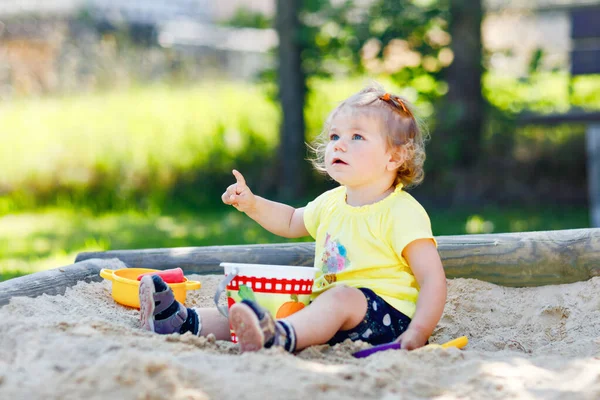 Dışarıda parkta kumlarda oynayan tatlı bir kız çocuğu. Güneşli sıcak yaz gününde güzel bir bebek eğleniyor. Kum oyuncakları ve renkli kıyafetlerle mutlu sağlıklı bir çocuk.. — Stok fotoğraf