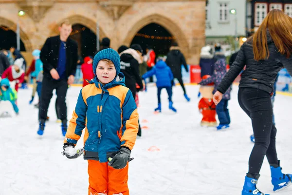 Gelukkige kleine jongen in kleurrijke warme kleren schaatsen op een ijsbaan van de kerstmarkt of kermis. Gezond kind dat plezier heeft op schaatsen. Veel mensen vieren vakantie en hebben een actieve wintervakantie — Stockfoto