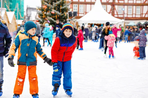 Dos niños felices con ropa de abrigo colorida patinando en una pista de mercado de Navidad o feria. Niños sanos, hermanos y mejores amigos se divierten en patinaje sobre hielo. Personas que tienen ocio activo de invierno —  Fotos de Stock
