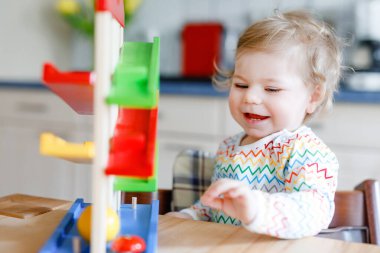 Küçük kız evde ya da çocuk odasında eğitici oyuncaklarla oynuyor. Mutlu sağlıklı çocuk renkli tahta top pisti ile eğleniyor. Çocuk top tutmayı ve yuvarlanmayı öğreniyor. Motorik eğitim.