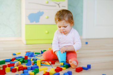 Eğitici oyuncaklarla oynayan tatlı küçük bir kız. Mutlu sağlıklı çocuk evde ya da çocuk odasında renkli tahta bloklarla eğleniyor. Bebek sürünüyor, renkleri ve biçimleri öğreniyor.