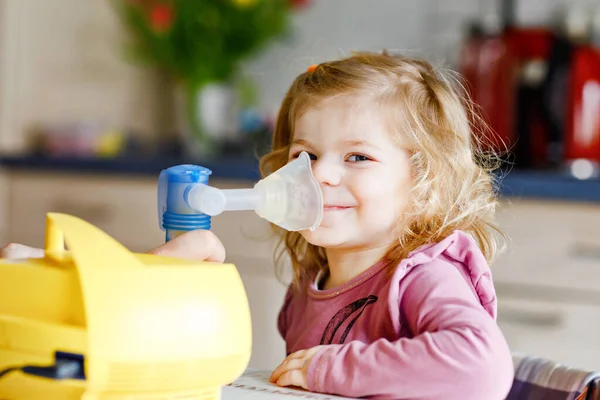自宅でネブライザーで吸入を作る小さな幼児の女の子。お父さんやお母さんが助けてデバイスを保持します。インフルエンザ、咳、気管支炎の子供。喘息吸入蒸気病気の概念 — ストック写真