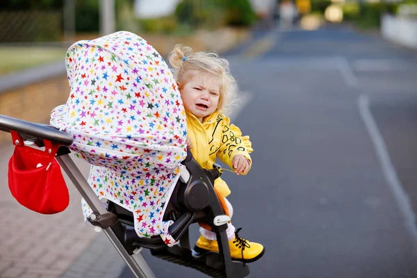 Retrato de una niña triste sentada en un cochecito y dando un paseo. El niño llorón no quiere sentarse en el cochecito. Hija sana. Crisis histérica de dos años fase — Foto de Stock