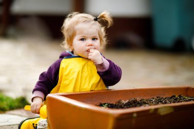 Bahar günü kum ve kürekle oynayan sevimli, tapılası bir kız. Sarı çizme ve çamur yağmurlu su birikintisi pantolon giyen bebek. Baharda sebze eken mutlu kız..