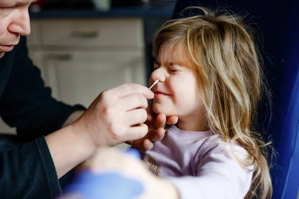 Vater macht nasale Heimat Coronavirus Geschmack zu kleinem Mädchen, Vorschulkind. Tochter und Vater nehmen Antigen-Test mit Wattestäbchen mit nach Hause. — Stockfoto