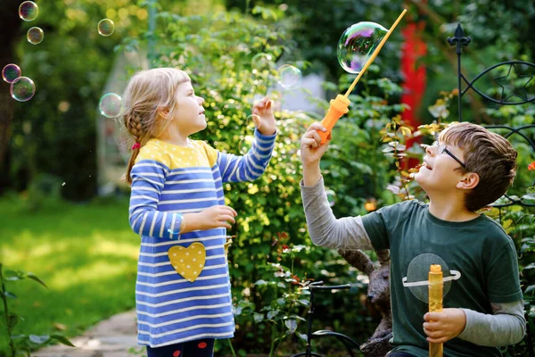 Fröhliche kleine Vorschulmädchen und Schulbuben haben Spaß mit dem Blasen von Seifenblasen. Kinder, liebe Geschwister, die zusammen spielen. Aktive lustige gesunde Kinder. Bruder und Schwester verliebt. — Stockfoto