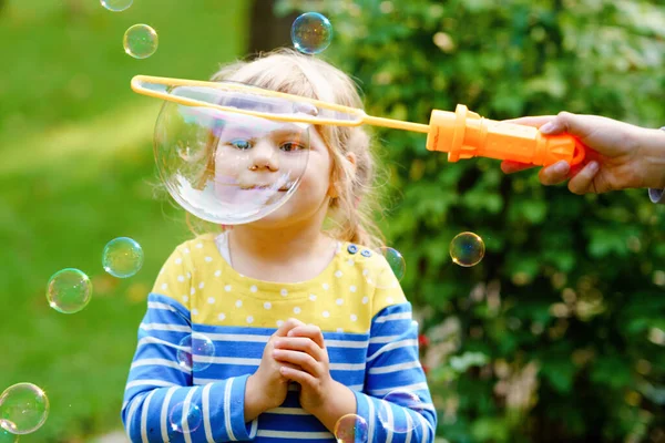Boldog kis szőke óvodás lány szórakozik szappanbuborék fúvóval. Aranyos gyerek játszik a napos nyári napon. Boldog, aktív, vicces, egészséges gyereket. Tevékenység gyermekek számára. — Stock Fotó