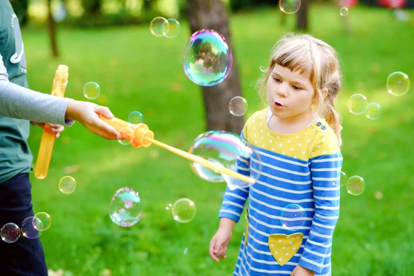 Happy little preschool girl and school kid boy having fun with blowing soap bolla blower. Bambini, adorabili fratelli che giocano insieme. Bambini sani divertenti attivi. Fratello e sorella innamorati. — Foto Stock