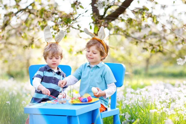 Dois meninos vestindo orelhas de coelho da Páscoa, pintando ovo colorido — Fotografia de Stock