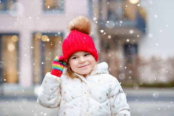 Funny portrait of little preschool girl in winter clothes. Happy positive child with red hat and colorful gloves outdoors. Winter day. — Stock Photo, Image