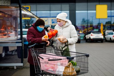 Kıdemli kadın ve tıbbi maskeli sosyal hizmetler görevlisi pandemik koronavirüs hastalığı nedeniyle. Kızı ya da torunu süpermarkette alışveriş yaparken büyükannesine yardım ediyor, market arabasında yiyecek satıyor, açık havada geziyor.