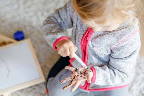 Крупный план малышки, изучающей живопись ручками для наконечников войлока. Маленький ребенок рисует на руках и одежде . — стоковое фото