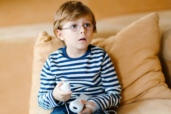 可爱的金发碧眼的小男孩带着眼镜玩电子游戏。在科罗纳病毒隔离检疫期间，孩子们在家里玩得很开心。孤独的男孩，没有朋友，呆在家里 — 图库照片