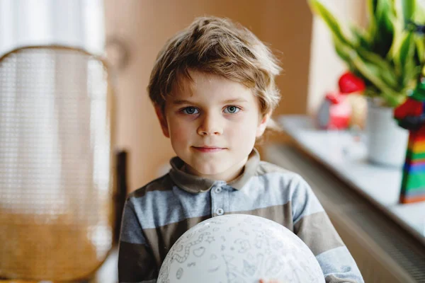 Little blond preschool kid boy with air balloon ball playing indoors at home or nursery. Funny child having fun alone. Happy childhood, kindergarden, school — Stock Photo, Image