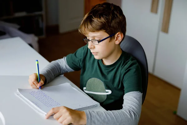 Kid boy with glasses learns at home for school. Preteen child making homework. Home schooling and distance learning concept. — 图库照片