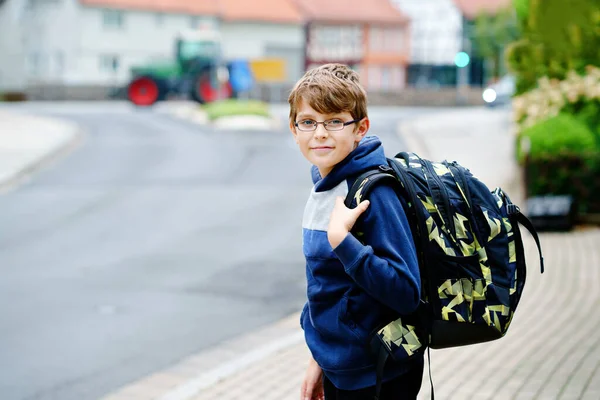 サッチェルと眼鏡をかけた幸せな子供の男の子。中学や高校に行く途中で眼鏡をかけている小学生。学校の庭の外で興奮した子供。学校に戻る. — ストック写真