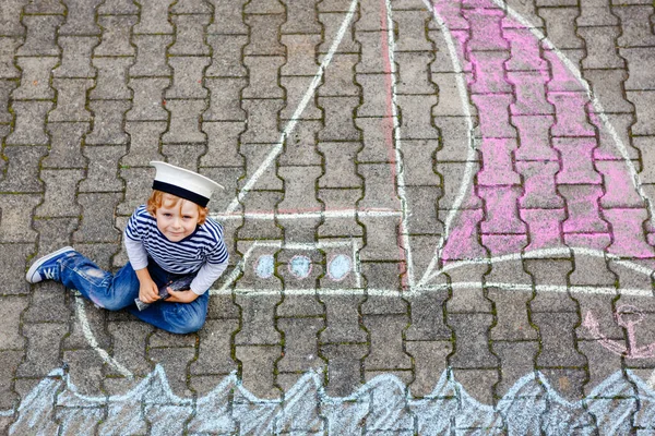 Petit garçon comme pirate sur le bateau ou voilier peinture d'image avec des craies colorées sur asphalte. Loisirs créatifs pour les enfants à l'extérieur en été. Enfant avec chapeau de capitaine et jumelles . — Photo