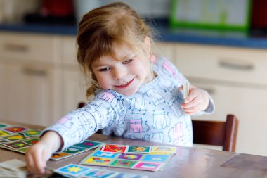 Heyecanlı, gülümseyen küçük kız iskambil oynuyor. Mutlu sağlıklı çocuk hafızasını eğitiyor, düşünüyor. Çocuk için evde yaratıcı bir eğlence ve eğitim. Evde aile aktivitesi.