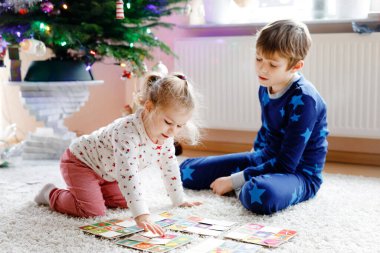 İki küçük çocuk, küçük tatlı kız ve okul çocuğu süslü Noel ağacında kağıt oynuyorlar. Mutlu sağlıklı kardeşler, erkek ve kız kardeşler birlikte eğleniyor. Aile Xmas kutlaması