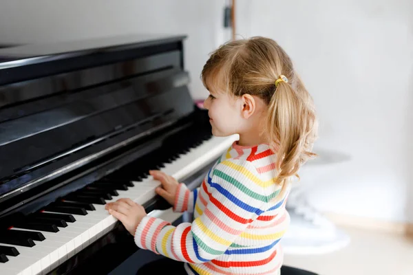 Menina pequena bonita tocando piano na sala de estar. Criança pré-escolar bonito se divertindo com a aprendizagem de tocar instrumento de música com conceito de aprendizagem durante o bloqueio do vírus corona homeschooling. — Fotografia de Stock