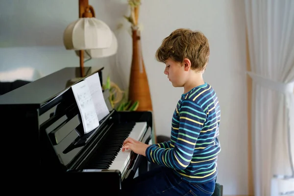 Hermoso niño tocando el piano en la sala de estar. Niño divertirse con el aprendizaje de tocar el instrumento de música con la aplicación de la tableta. Concepto de aprendizaje electrónico durante el bloqueo del virus corona de la educación en el hogar. — Foto de Stock