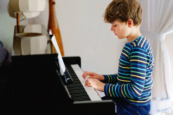 Hermoso niño tocando el piano en la sala de estar. Niño divertirse con el aprendizaje de tocar el instrumento de música con la aplicación de la tableta. Concepto de aprendizaje electrónico durante el bloqueo del virus corona de la educación en el hogar. —  Fotos de Stock