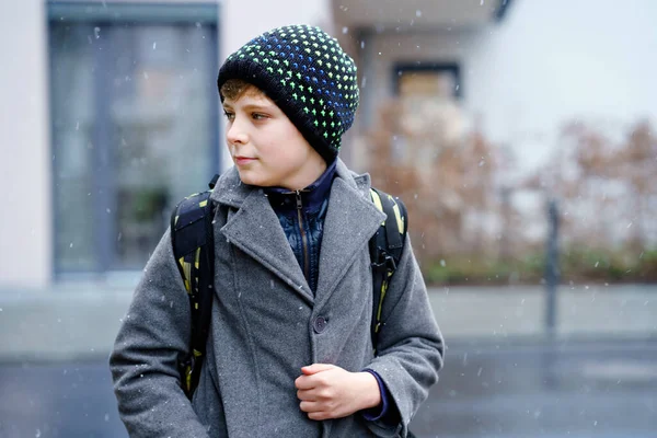 Retrato de un niño preadolescente al aire libre. Niño guapo en abrigo y sombrero en invierno. Escolar en el camino a la escuela con mochila durante la nieve —  Fotos de Stock