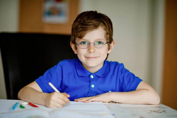 Портрет маленького мальчика в очках дома, делающего домашнее задание, пишущего письма красочными ручками. Маленький ребенок занимается спортом в помещении. Начальная школа и образование, концепция домашнего обучения. — стоковое фото